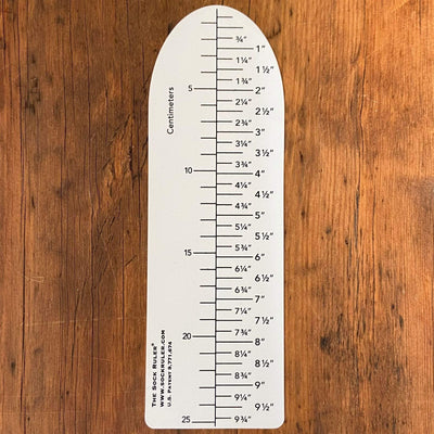 The Sock Ruler in a size medium on a wood table. 