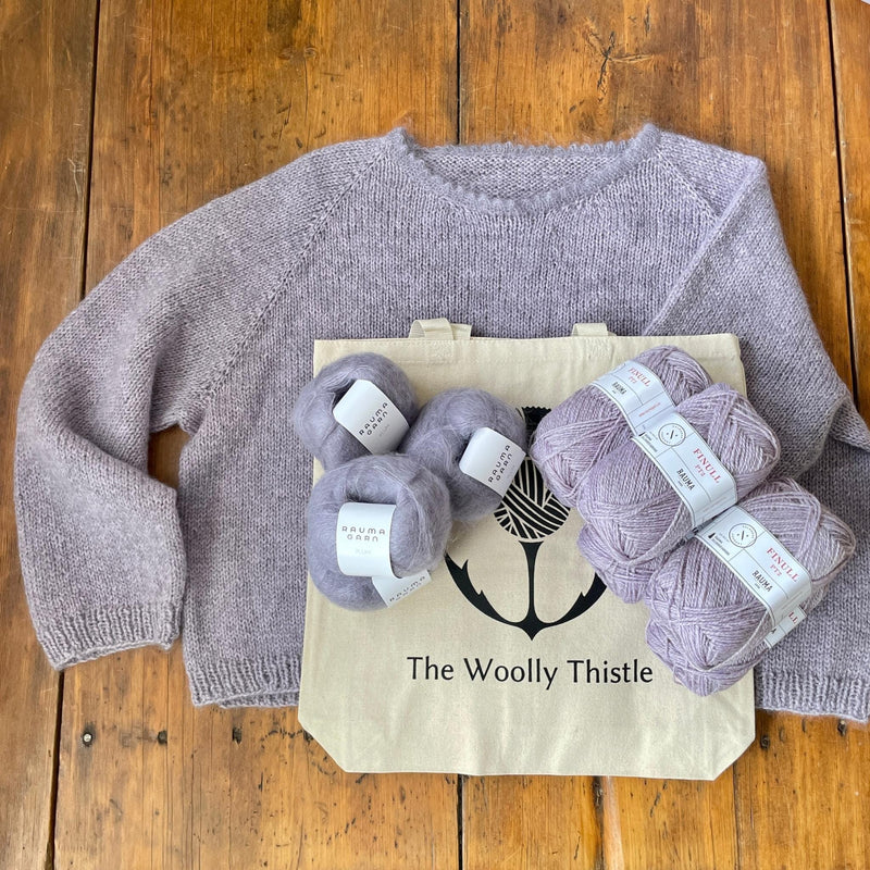 Light Purple sweater on wooden table with The Woolly Thistle tote bag and balls of yarn in light purple Rauma Finullgarn and Plum