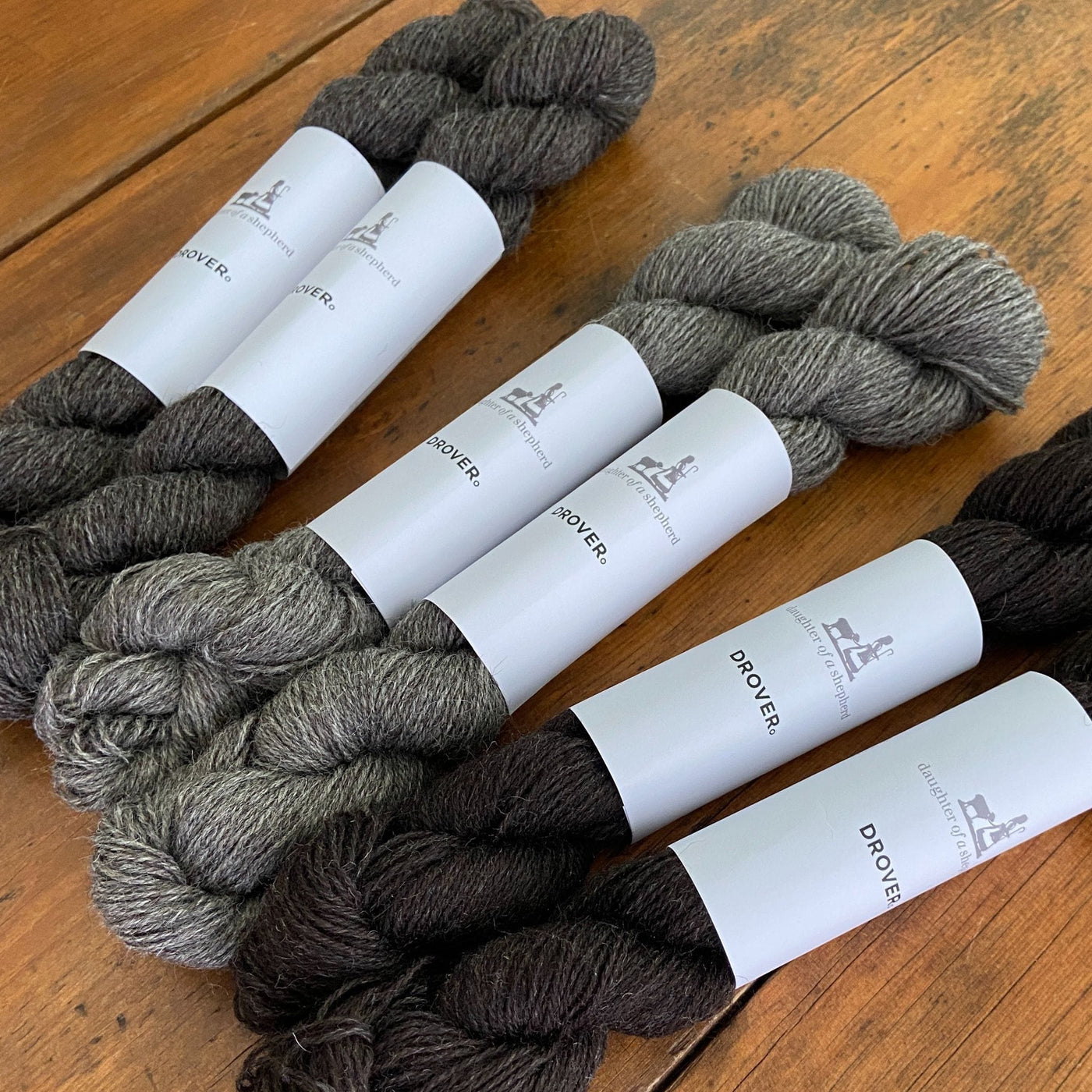 Skeins of Daughter of a Shepherd Drover yarn in shades of grey on table.