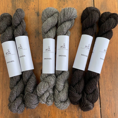 Skeins of Daughter of a Shepherd Drover yarn in three shades of grey lying on wooden table.