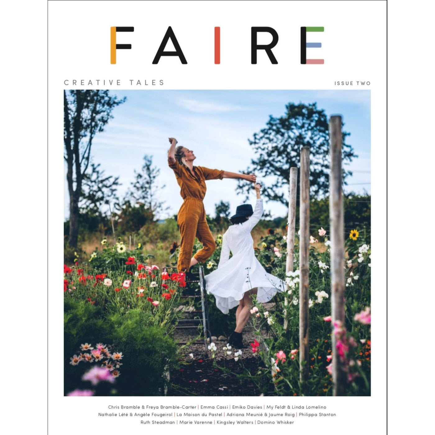 The cover of Faire Issue two features two white women dancing in a flower garden on a sunny day.