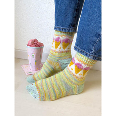 Two feet wearing socks in shades of pastel with a pink ice cream cone colorwork motif, near a cup of ice cream