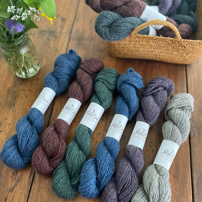 Jagger Spun Gotland Yarn in 6 colors on wooden table with basket of yarn in background. 