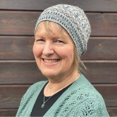 Linda Shearer, designer of the Bonnie Isle Hat pattern, is shown wearing the Bonnie Isle Hat. She is the Shetland Wool Week 2022 patron. 