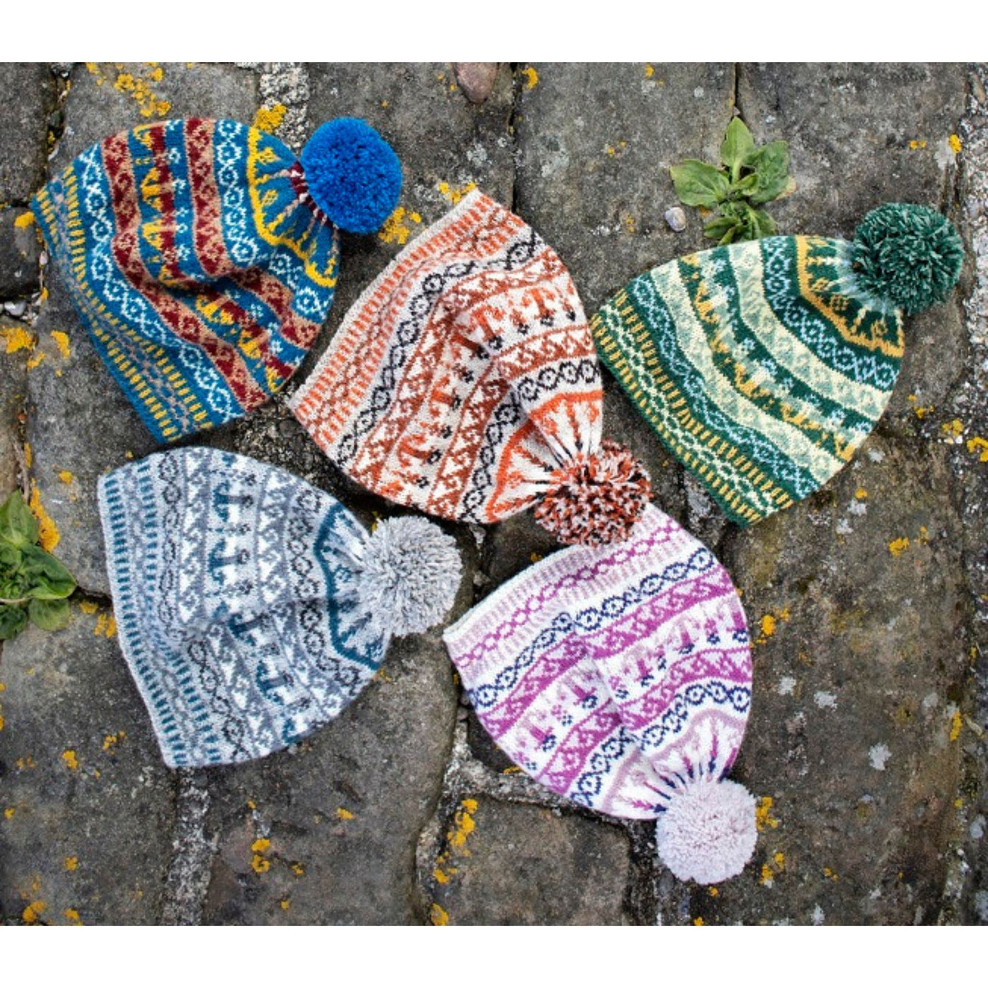 5 Bonnie Isle Hats knit in 5 different colorways are lying on rocks.