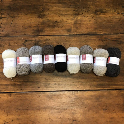 An array of balls of Jamieson & Smith Shetland Supreme, a fingering weight wool yarn, in various colors, on a wooden table