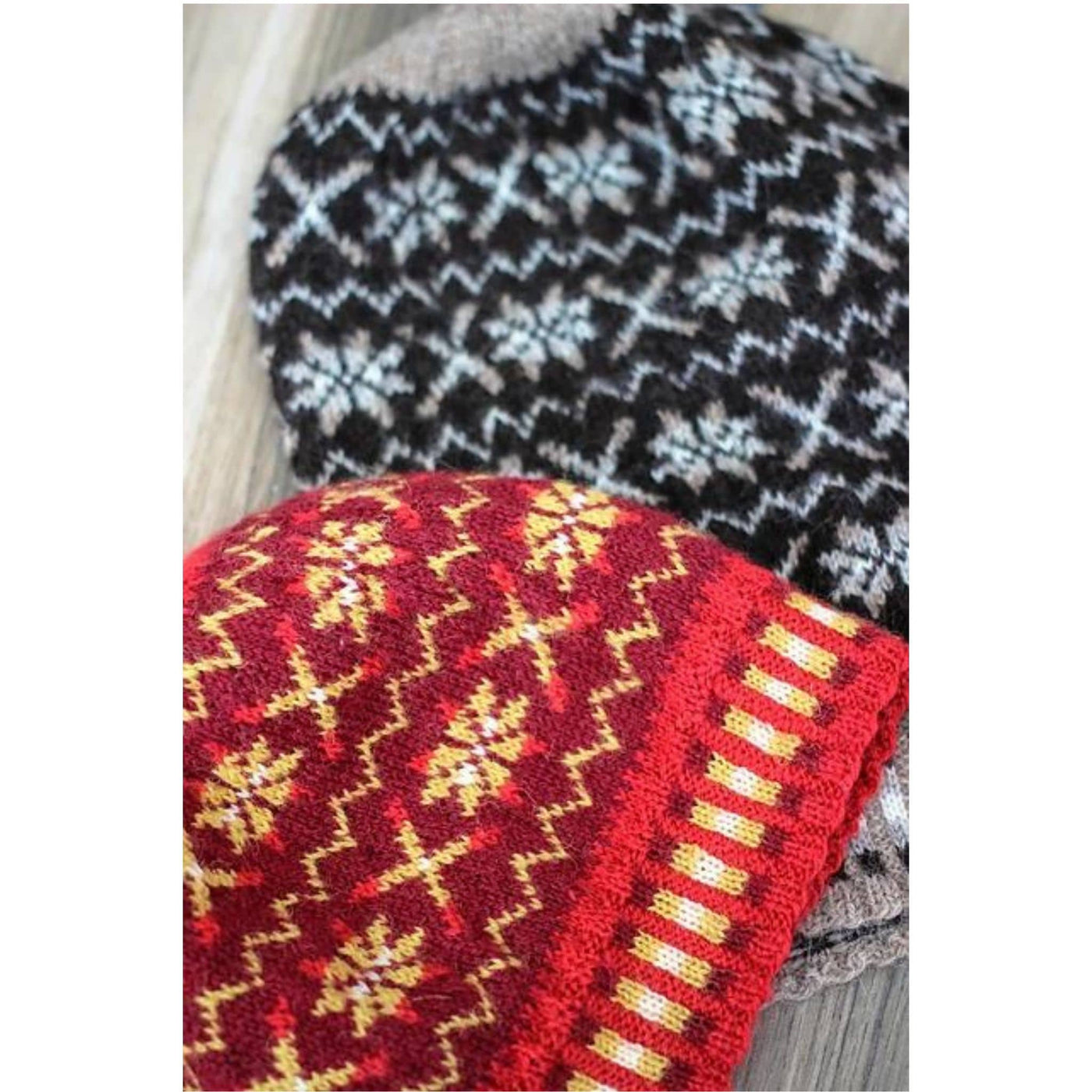 Two Fair Isle hats lying flat on table. One in Berry Wine colorway and one in Shetland Black colorway. Pattern is Tirval's Toorie (hat). Knit with Jamieson & Smith Heritage yarn. 