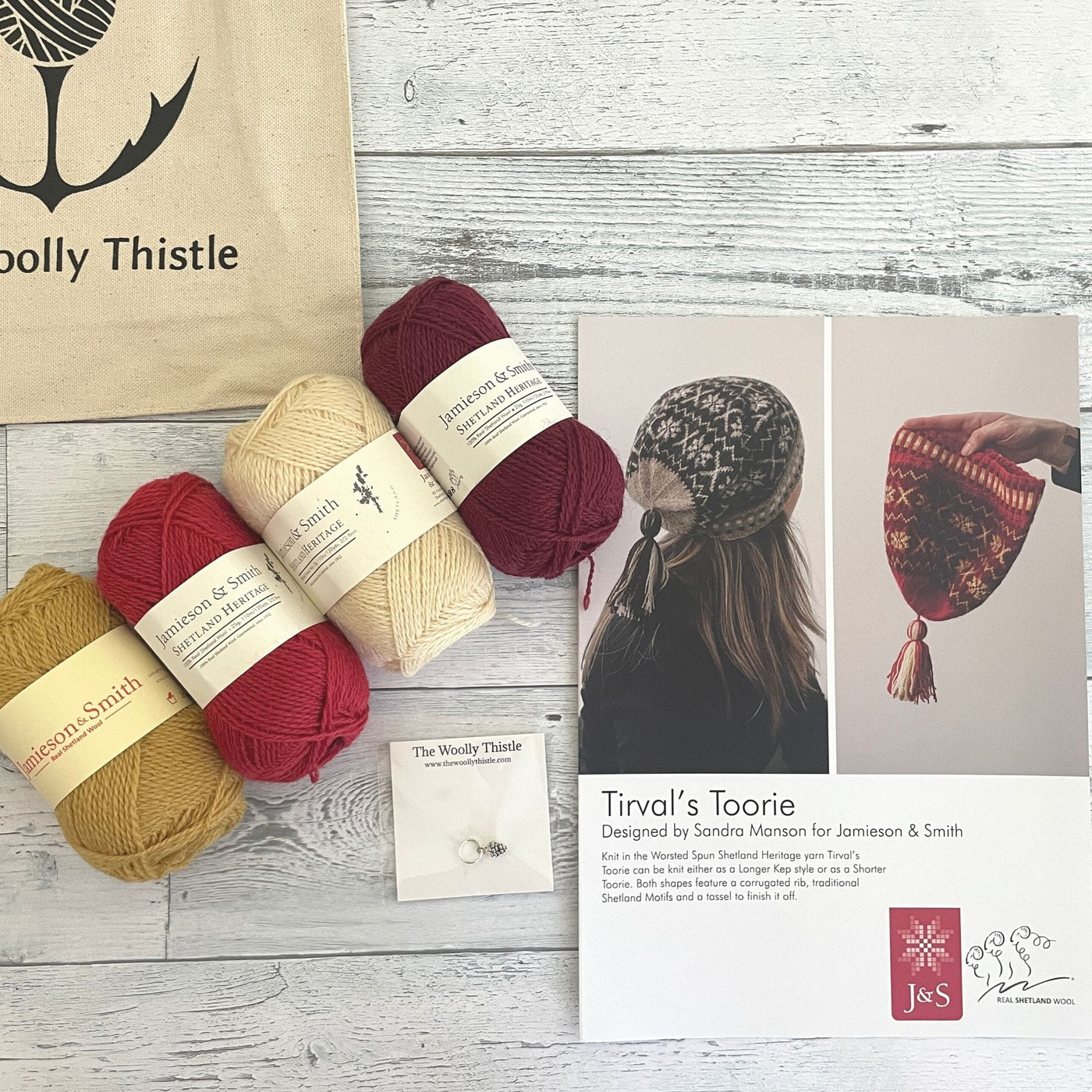 Components of the Tirval's Toorie Kit. Jamieson & Smith Heritage yarn in Berry, Wine colorway shown with The Woolly Thistle Tote Bag, Stitch Marker, and the printed pattern for Tirval's Toorie.. 