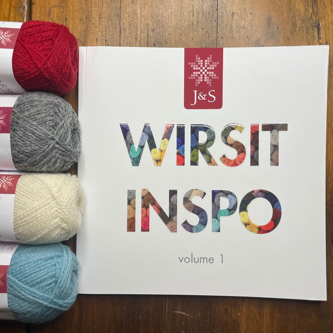 Wirsit Inspo Volume 1 from Jamieson & Smith. Cover of book is shown with several balls of Jamieson & Smith 2ply Jumper Weight yarn to the left of the book. 