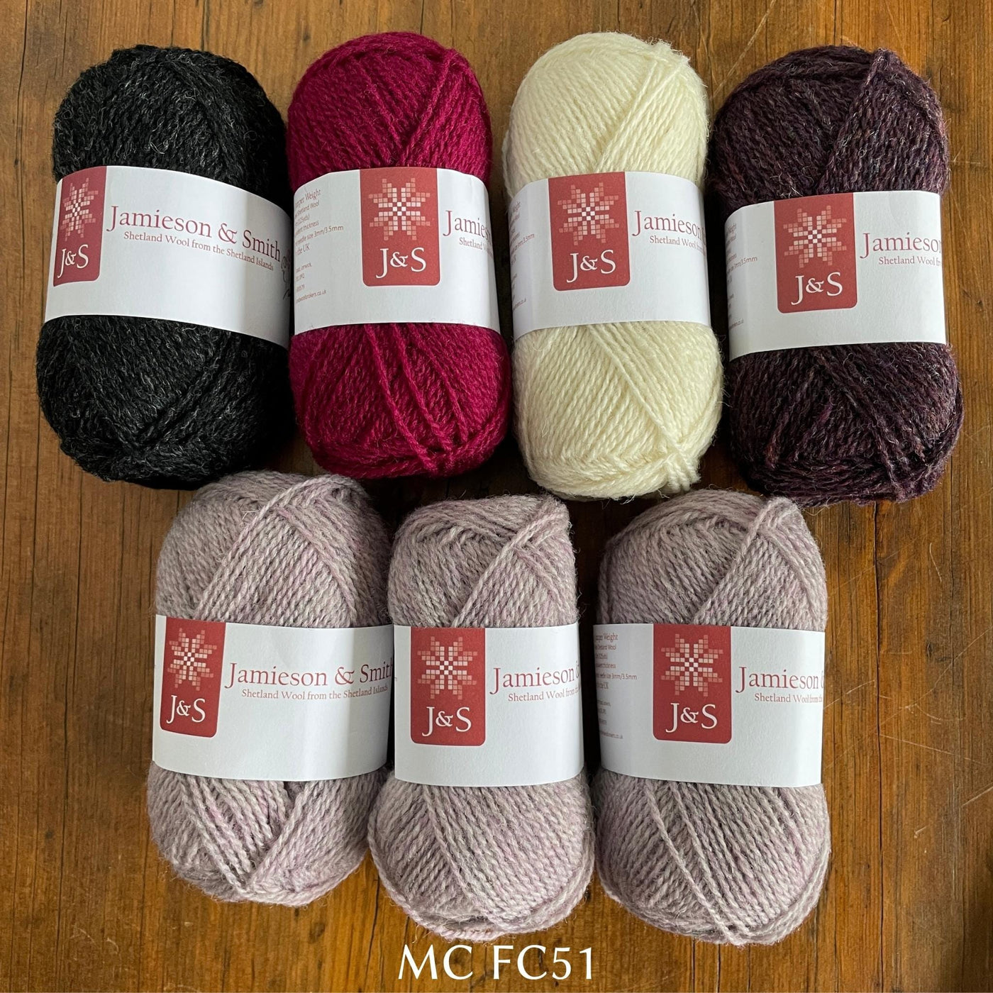 7 balls of J&S yarn in light cream/purple and dark grey, burgundy, red, and cream