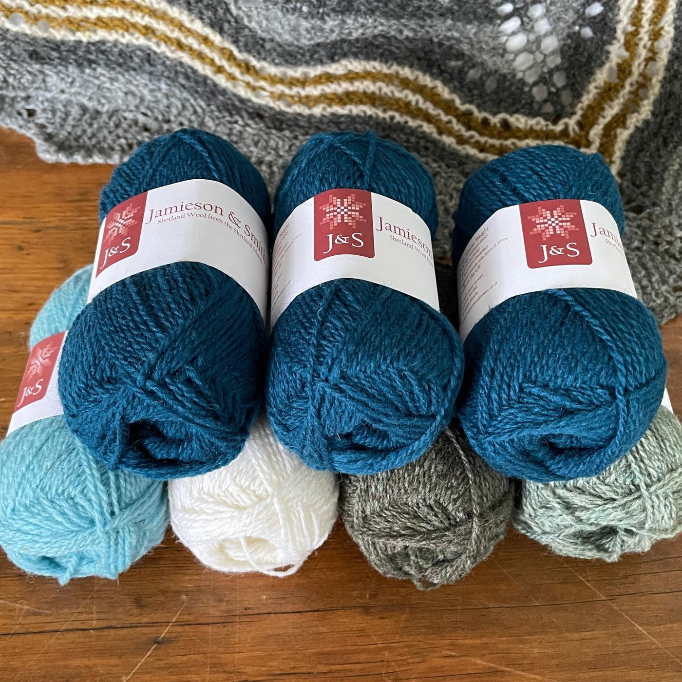 7 balls of J&S yarn in blue tones, grey and white.  knitted hap in background.