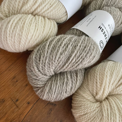 Three skeins of Junction Fiber Mill Farm Fresh, a DK weight yarn, in two natural colorways, on a wooden table