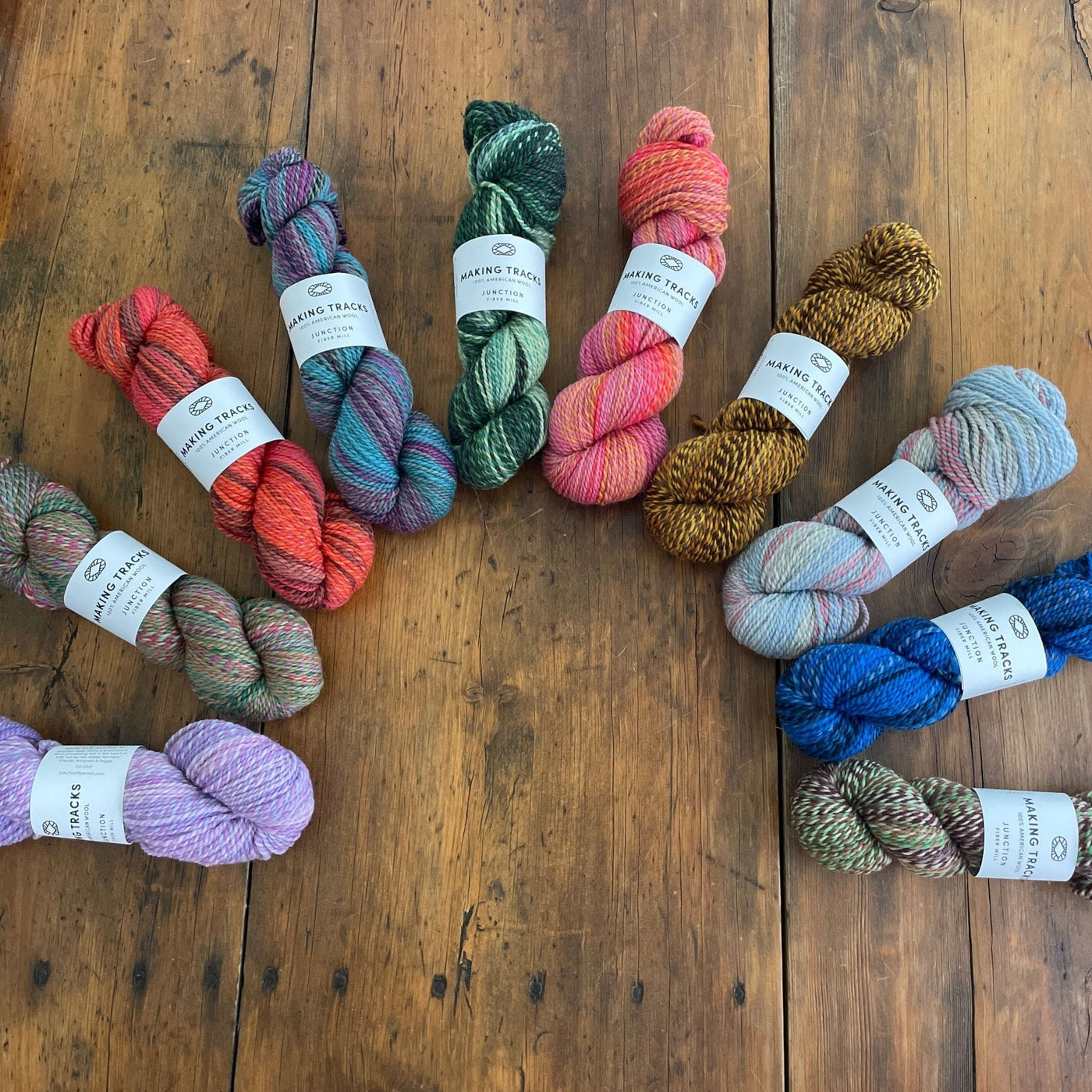 Ten skeins of Junction Fiber Mill Making Tracks yarn, a DK weight, barberpole yarn, in various colors, arrayed on a wooden table