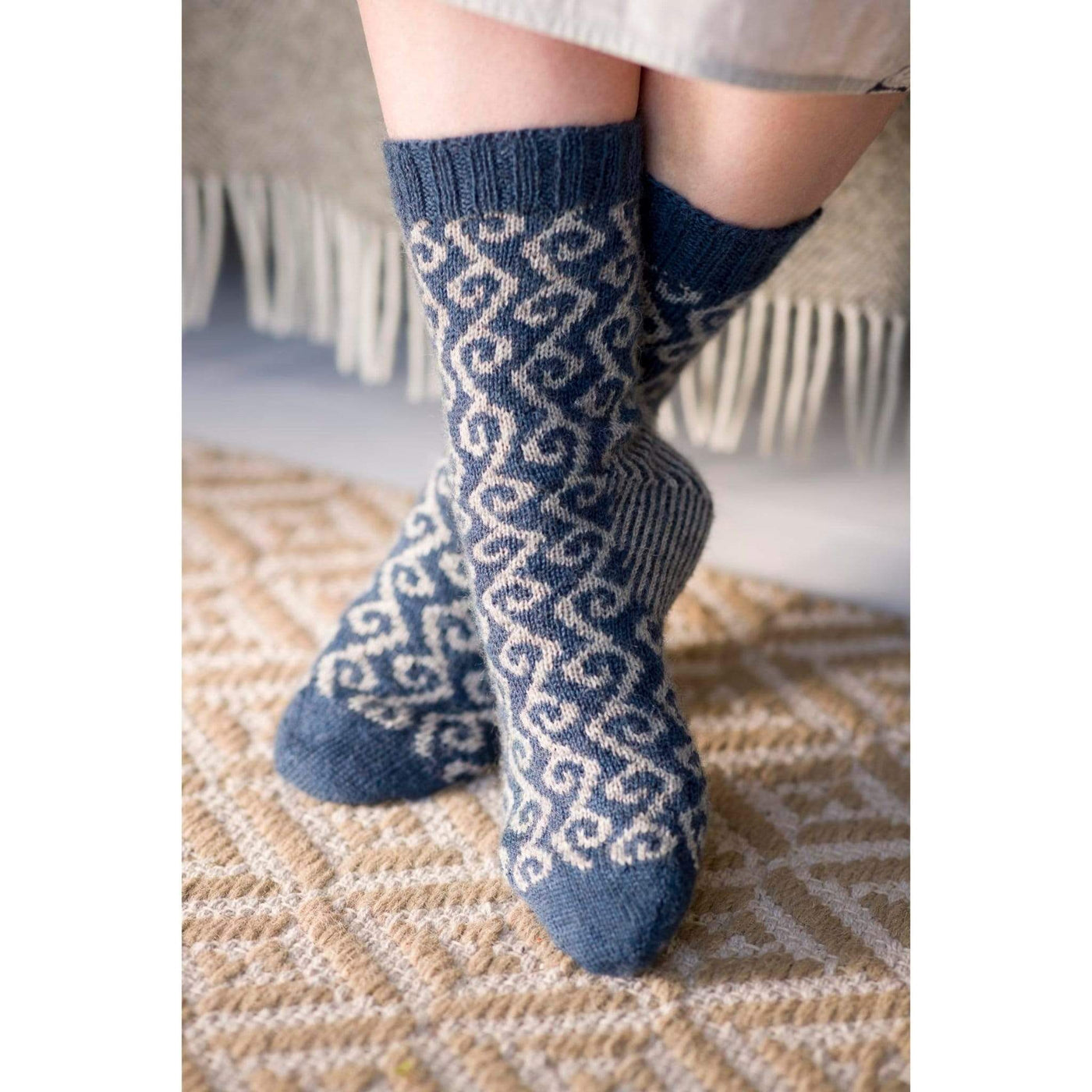 The Woolly Thistle Bluestockings by Kate Davies & Nicole Pohl featuring woman wearing blue and beige patterned long knitted socks