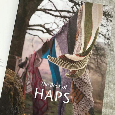 Inside of The Book of Haps by Kate Davies featuring many colorful Haps hanging on a clothesline.