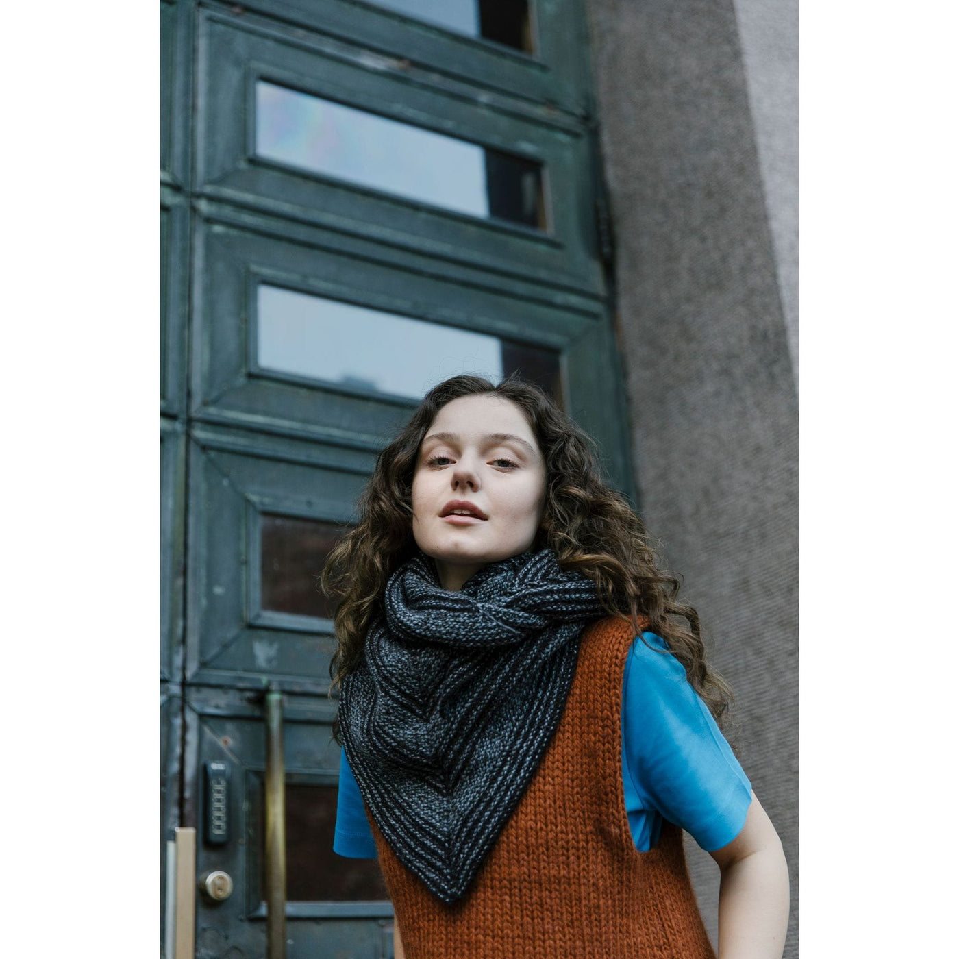 52 Weeks of Easy Knits page shows model wearing two of the knit designs in the book. Woman is standing in front of green door wearing a grey and black shawl scarf and an orange handknit vest. 