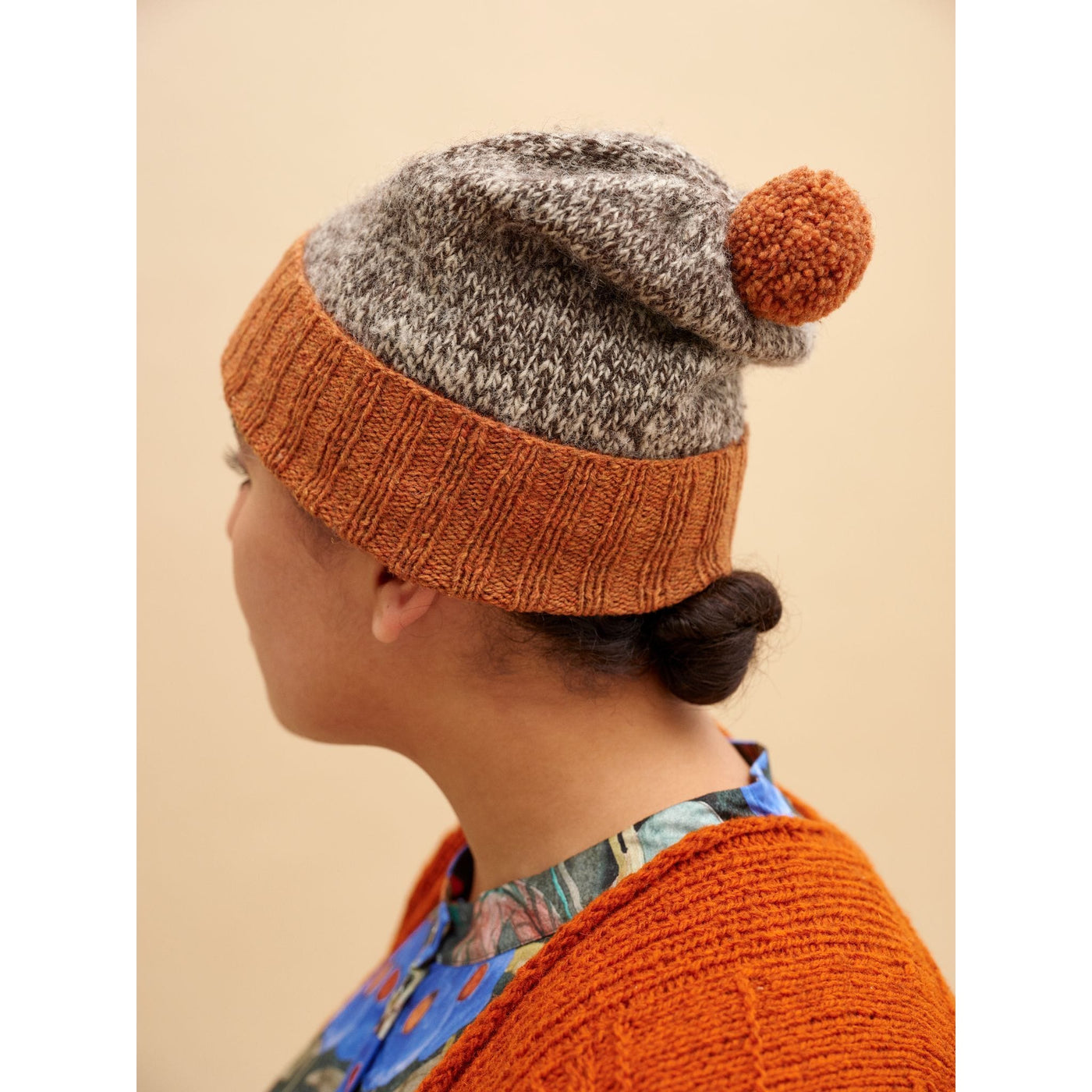 52 Weeks of Easy Knits page shows model wearing one of the knit designs in the book. Side/Back view of the model wearing a grey and orange hat with a folded brim and orange pom pom.  