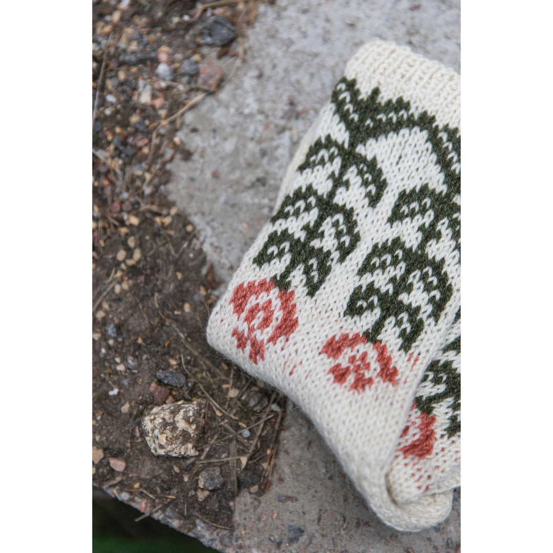Knitted Kalevala book by Jenna Kostet from Laine Publishing. A design from book shows colorwork socks, folded on rock, with flowers knit in cream, green, and coral.
