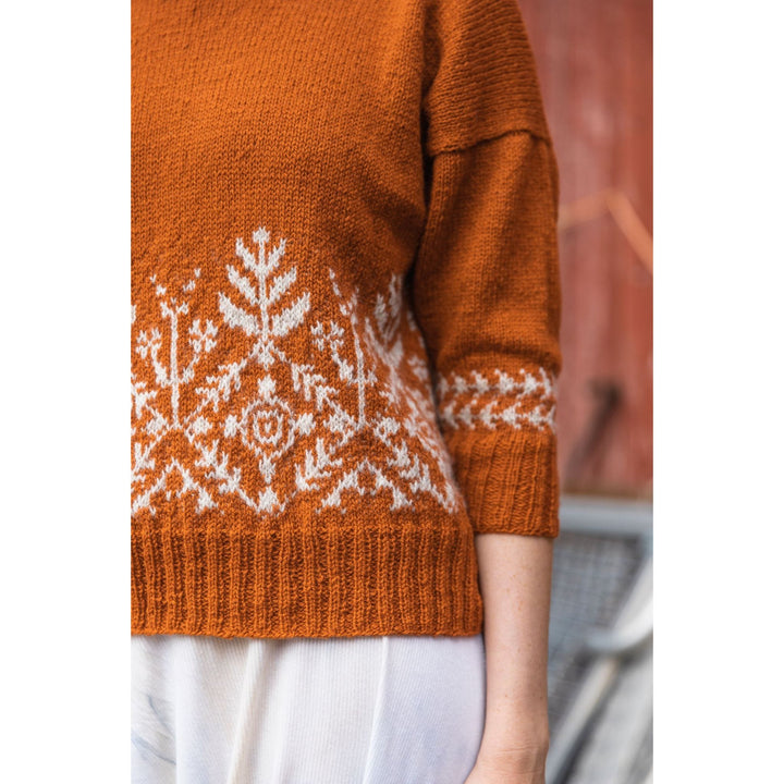Knitted Kalevala book by Jenna Kostet from Laine Publishing. A design from book is shown with colorwork lower body of sweater knit in orange and cream..