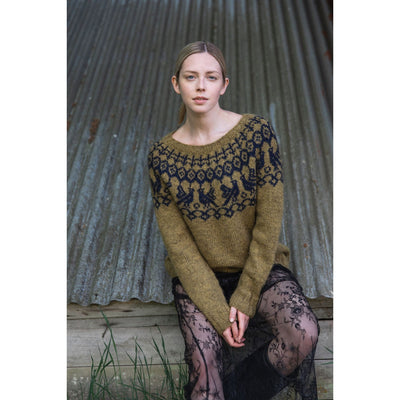 Knitted Kalevala book by Jenna Kostet from Laine Publishing. A design from book is shown - model sitting outside wearing gold and black colorwork yoke.