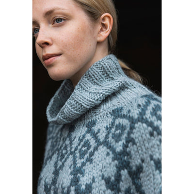 Knitted Kalevala book by Jenna Kostet from Laine Publishing. A design from book is shown - side top view of model wearing colorwork sweater in two shades of blue.
