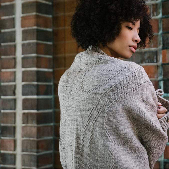 Model photographed from behind wearing a gray knit garment with textured curved lines.