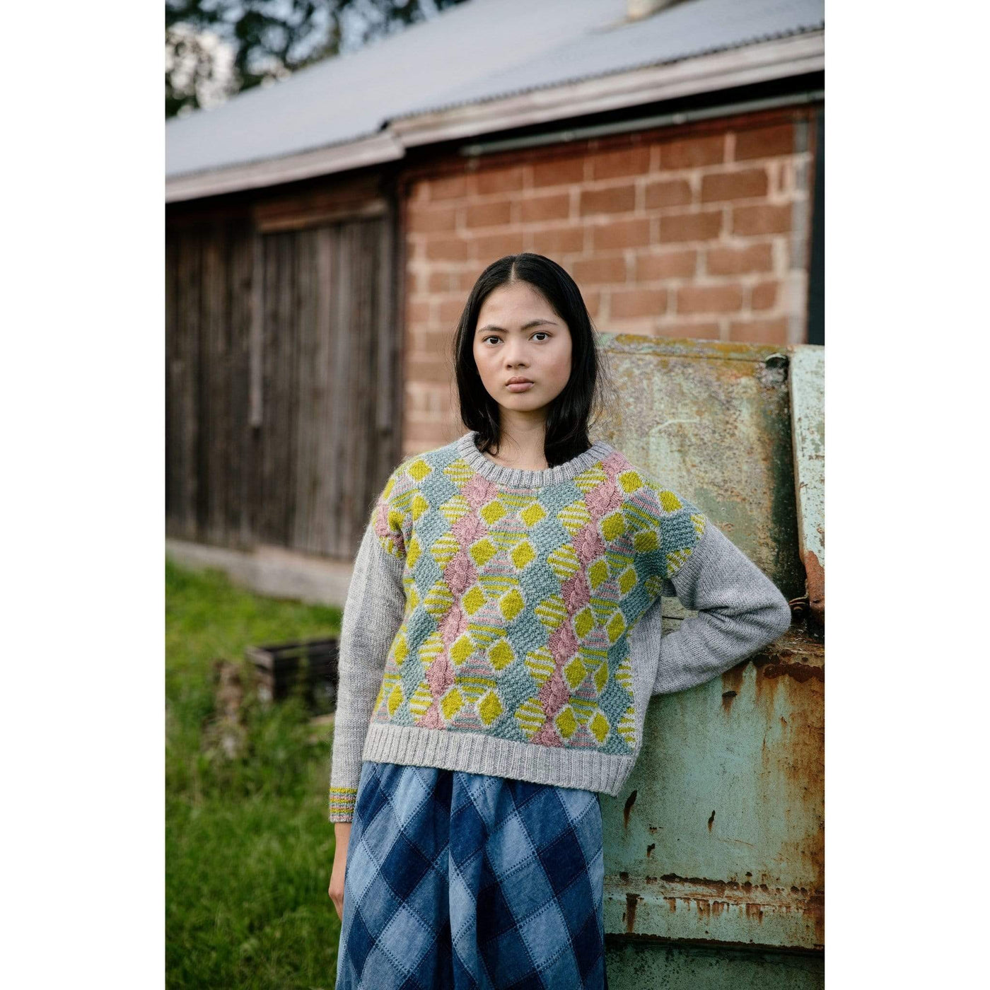 The Woolly Thistle Worsted – A Knitwear Collection Curated by Aimée Gille of La Bien Aimée published by Laine woman wearing grey knitted sweater with yellow, blue, and pink design in the front