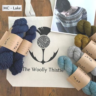 Components of the Lunenburg Pullover by Amy Christoffers yarn set, Lichen and Lace Rustic Sport weight yarn in 5 colors wit Lake, a dark blue (Lake) as the main color, shown with The Woolly Thistle Tote Bag.