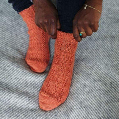 Model pulling on orange cable knit socks.