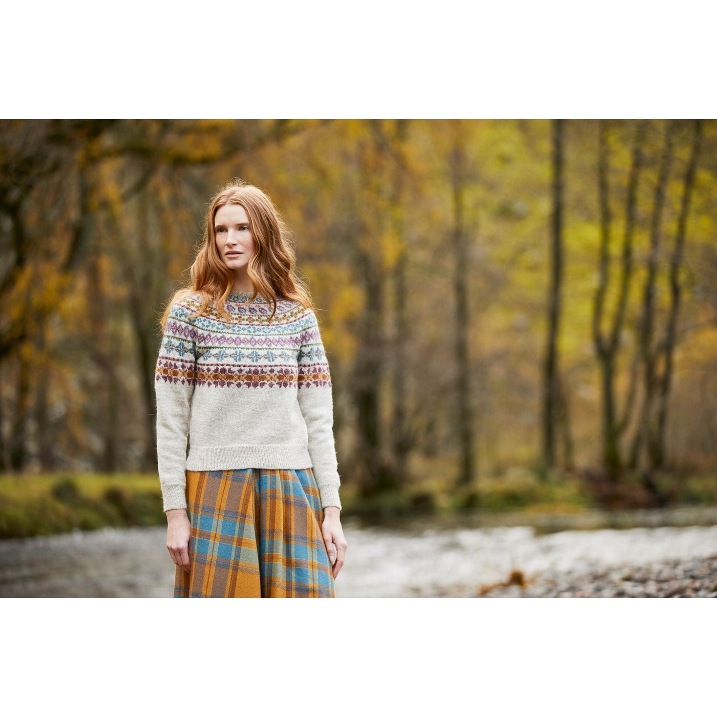 model standing outside wearing Catbells Sweater by Marie Wallin and a plaid skirt; main color of sweater is raw with multicolor design on top