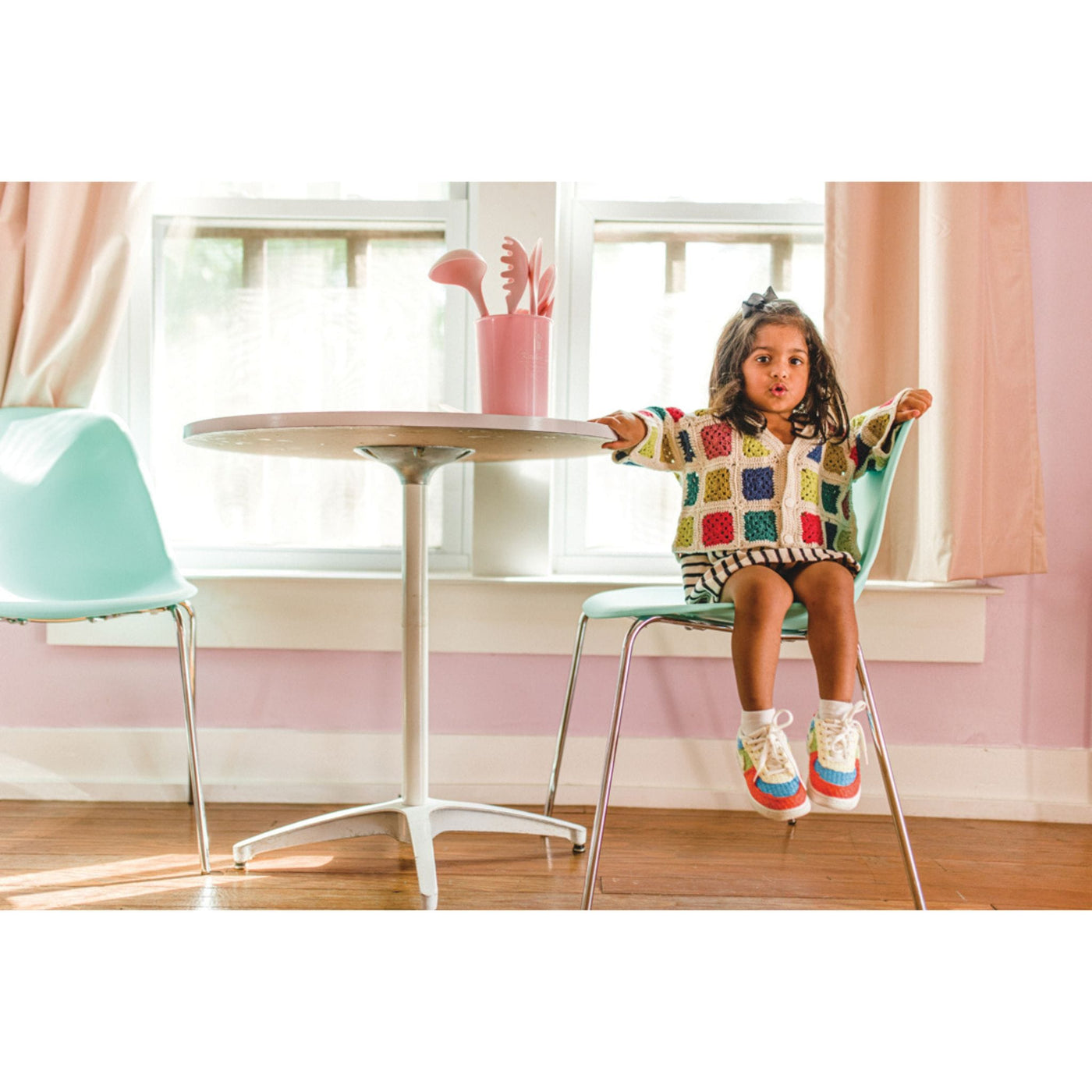 Child sitting in chair wearing a cardigan with colorful blocks. Sweater is a design from Mini Pom Magazine. 
