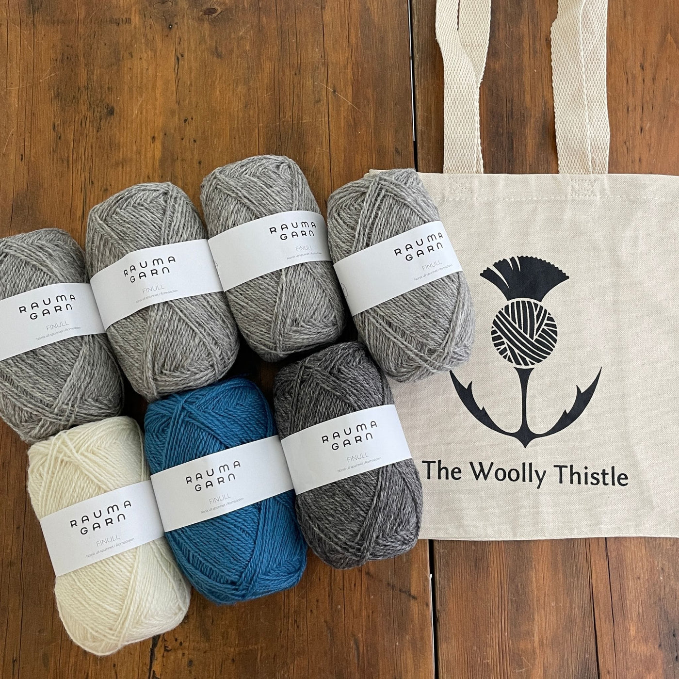 Components of the Varde Skirt Kit including TWT Tote, and Rauma Finullgarn yarn in greys and blue.