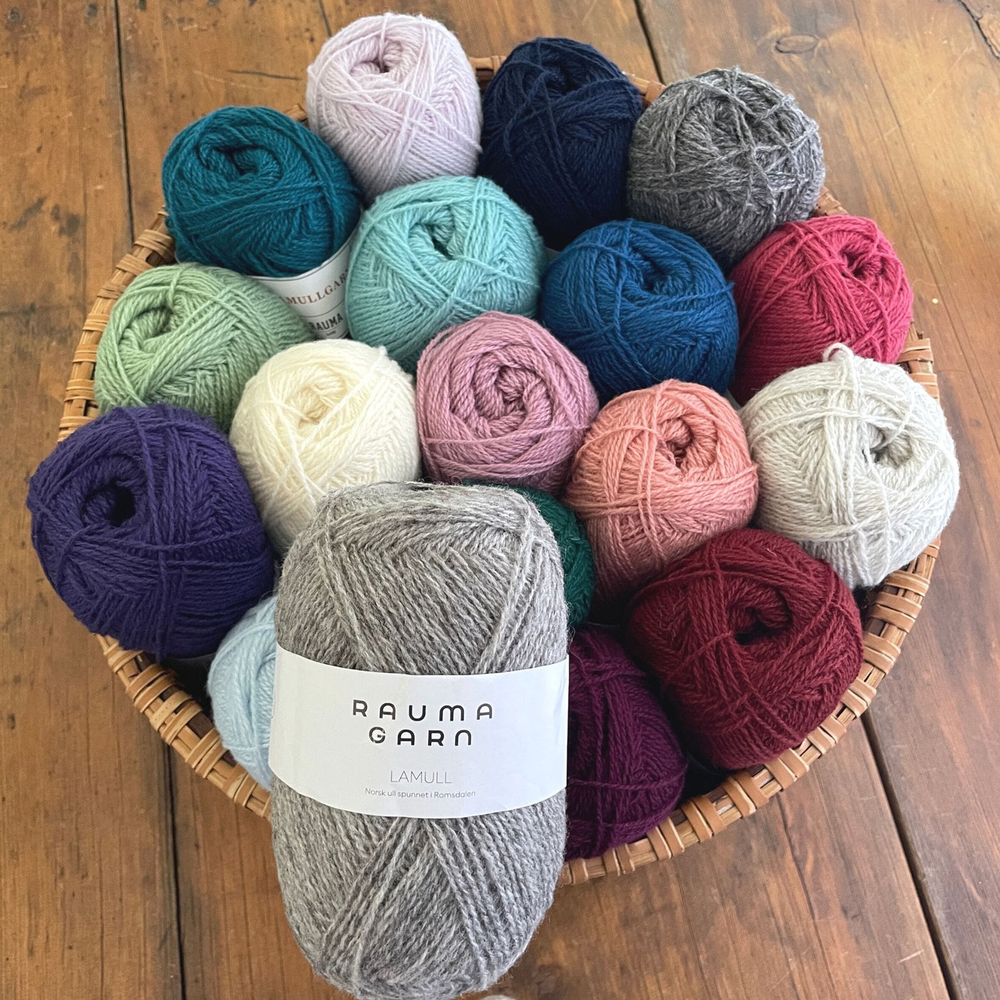A basket filled with a variety of skeins of Rauma Lamullgarn fingering weight wool yarn.