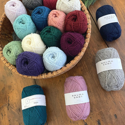 A basket of balls of Rauma Lamullgarn, a fingering weight yarn, on a table with four more balls of Lamullgarn