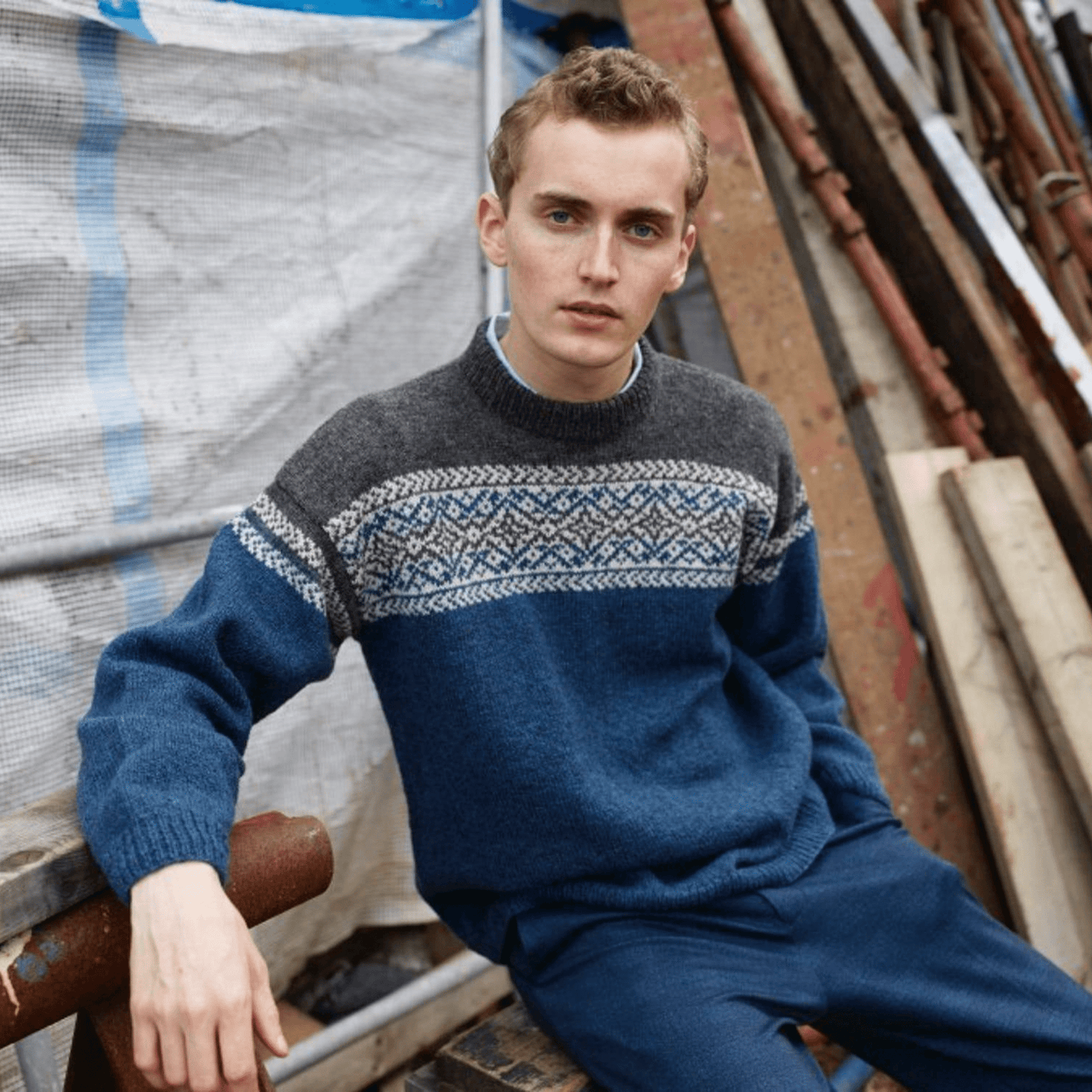 Man wearing knitted blue, cream and grey patterned sweater from Rauma Finullgarn  pattern book from the Woolly Thistle