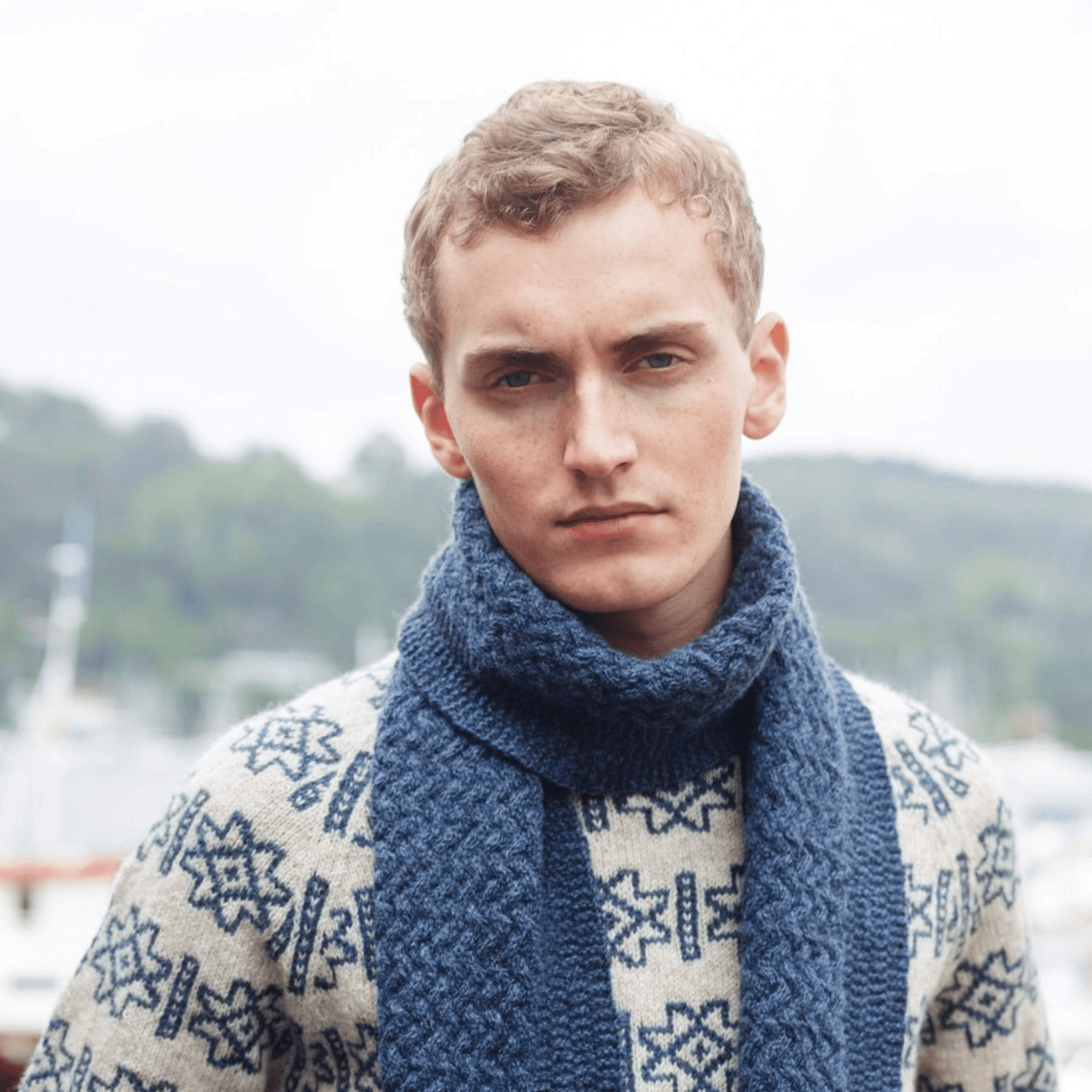 Man wearing knitted tan and blue patterned sweater and blue scarf from Rauma Finullgarn pattern book from the Woolly Thistle