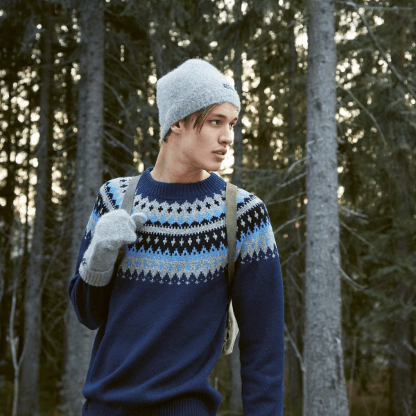 Man wearing knitted blue and grey patterned sweater and knitted grey hat and gloves from Rauma Finullgarn Varde pattern book from the Woolly Thistle