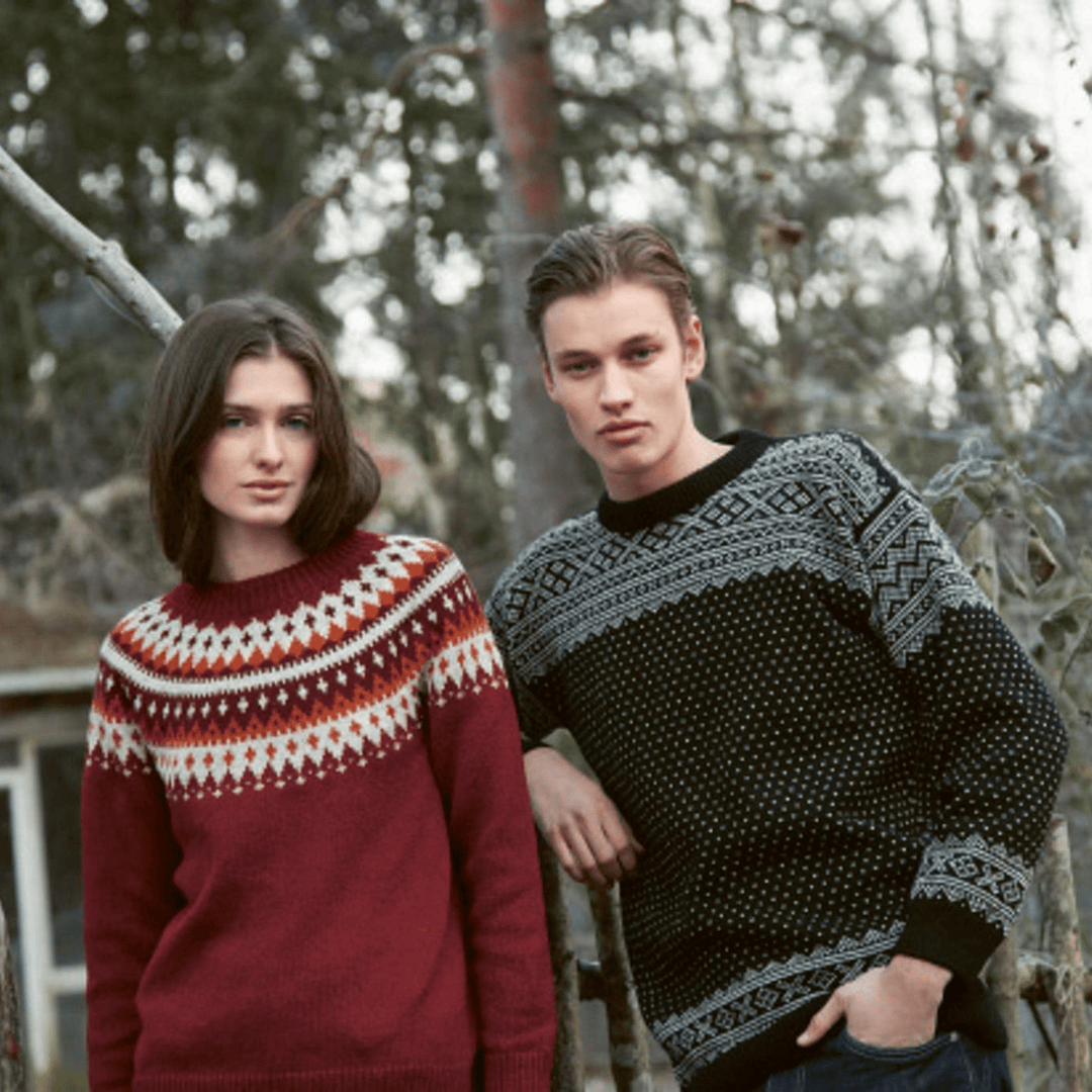 Woman wearing knitted red sweater with pattern and man wearing knitted black sweater with pattern from Rauma Finullgarn Varde pattern book from the Woolly Thistle