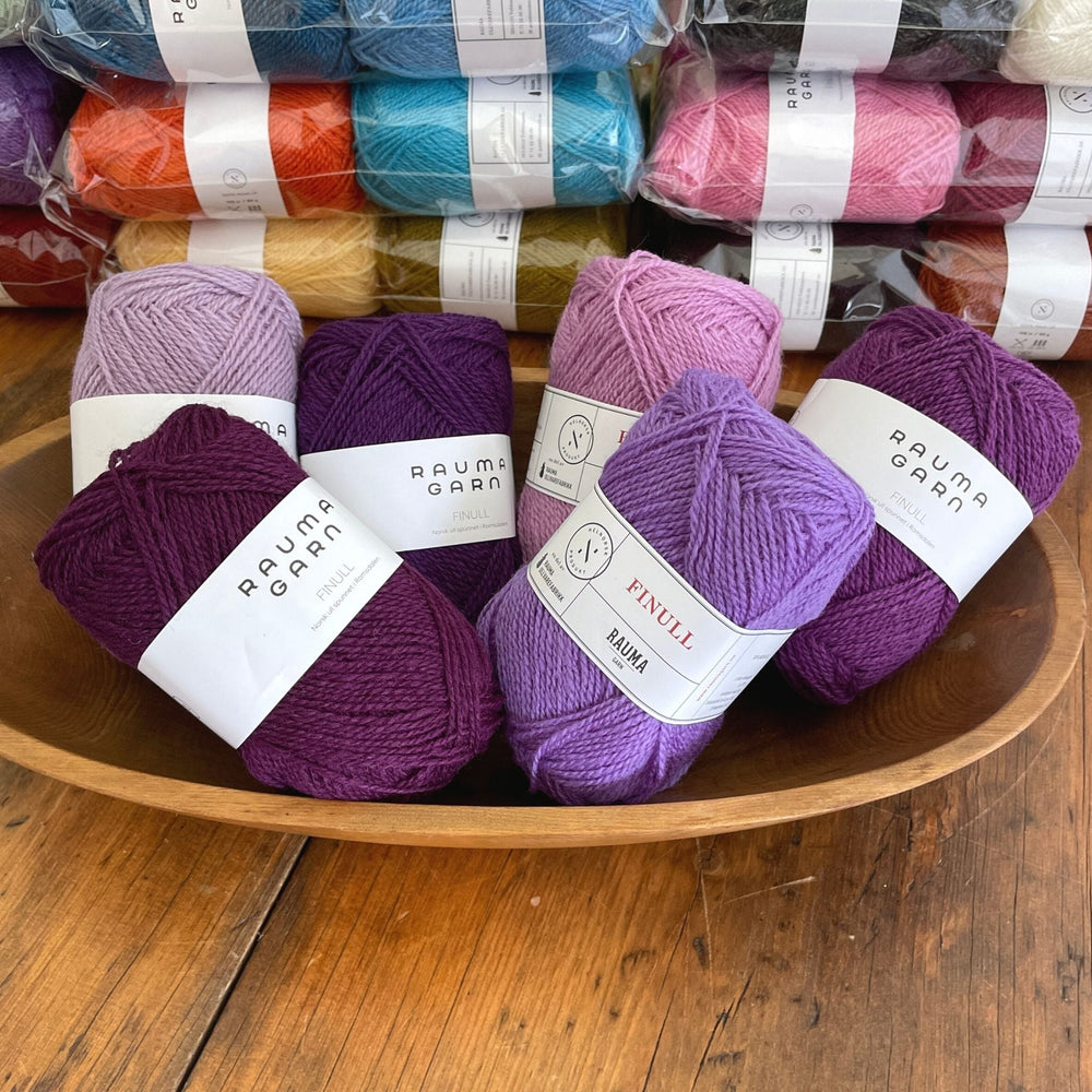 A colorful selection of Rauma Finullgarn 6 packs of yarn including a bowl filled with various purple shades.