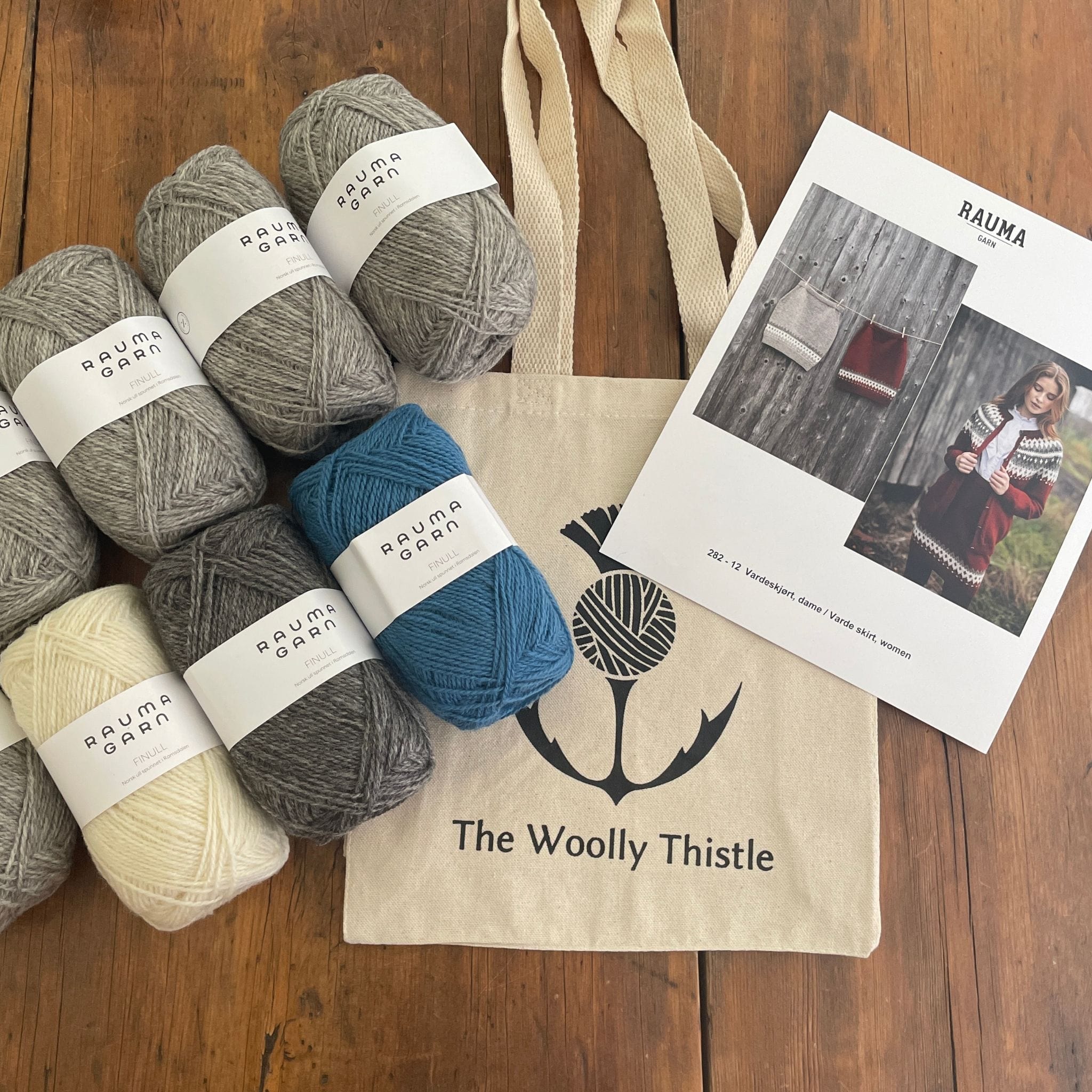 Components of the Varde Skirt Kit including pattern card, TWT Tote, and Rauma Finullgarn yarn in greys and blue.