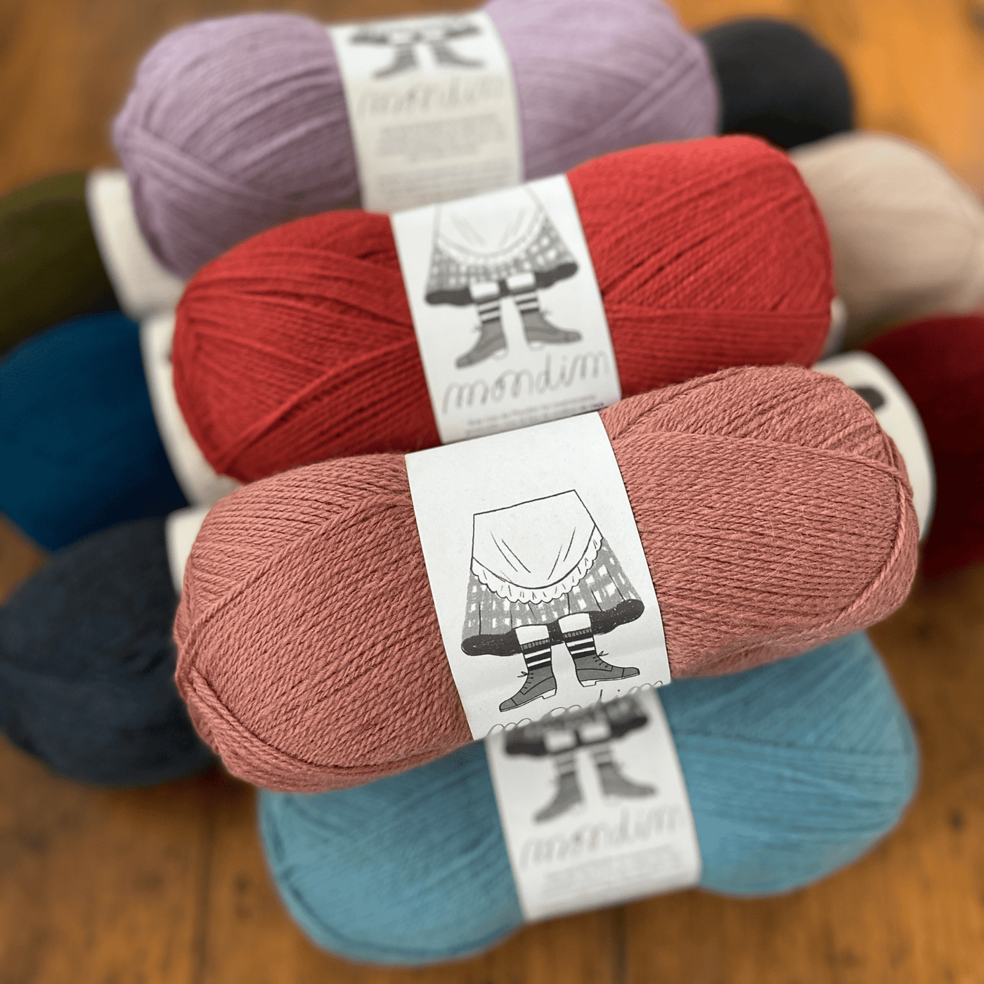 The Woolly Thistle Retrosaria Mondim Fingering Weight Yarn in multiple colors like pink, red, purple, blue, green, cream, black, burgundy, and more