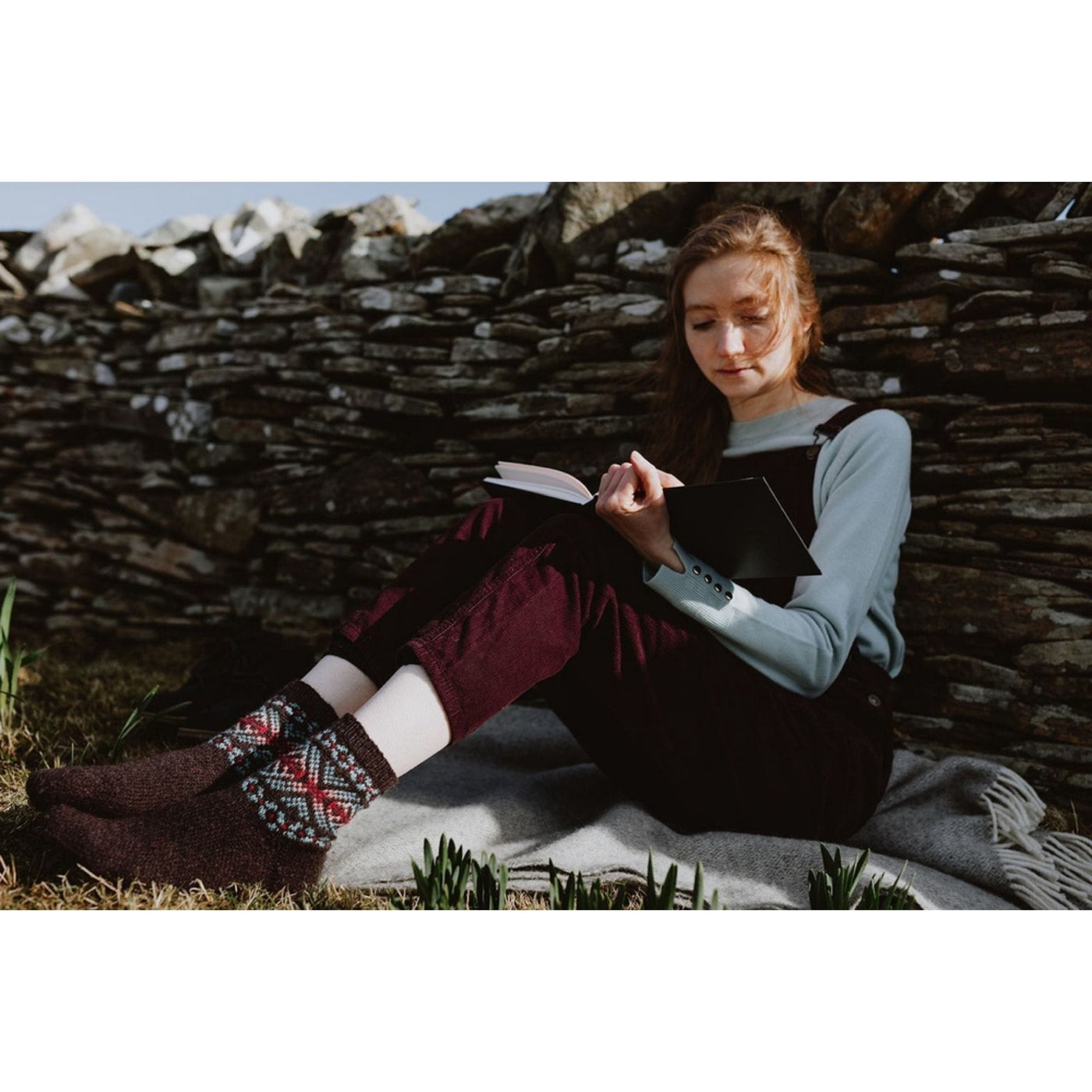 Page of Shetland Wool Adventure Journal 4, showing woman reading with colorwork socks showcasing a pattern in the book. 