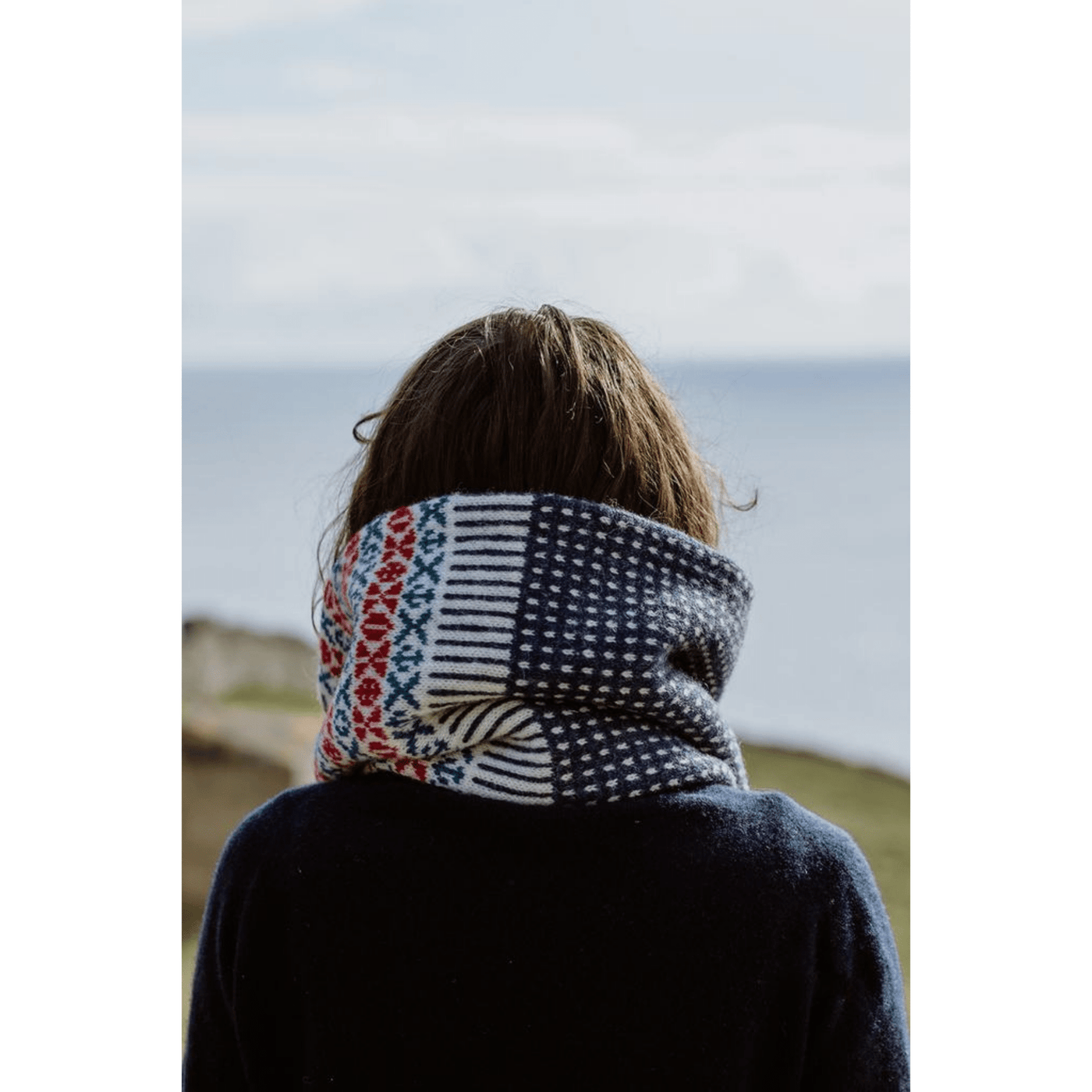 The Woolly Thistle image from Shetland Wool Week Annual 2021 featuring a woman looking at the ocean wearing knitted scarf 