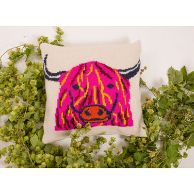 Pillow or cushion with Highland Cow design embroidered in pink. Greenery arranged around pillow. 