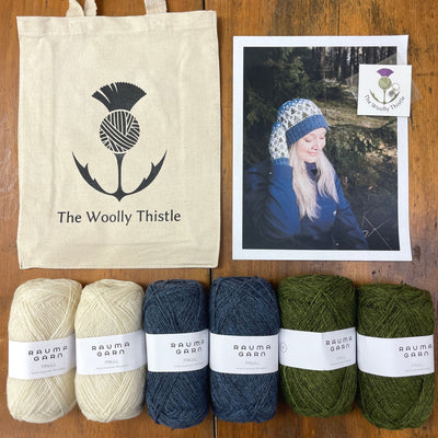 Components of the Heart of the Forest Mittens and Hat Yarn Set. Shown with a photo of the knit items and Rauma Finullgarn yarn in heathered blue, cream, and green. Six balls of yarn are lined up along bottom of frame. The Woolly Thistle Stitch Marker and Tote Bag are shown on top with a photo woman wearing the knitted hat and mittens.