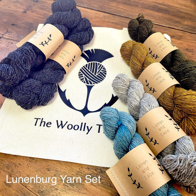 Components of the Lunenburg Pullover by Amy Christoffers yarn set, Lichen and Lace Rustic Sport weight yarn in 5 colors wit Lake, a dark blue as the main color,  shown with The Woolly Thistle Tote Bag.