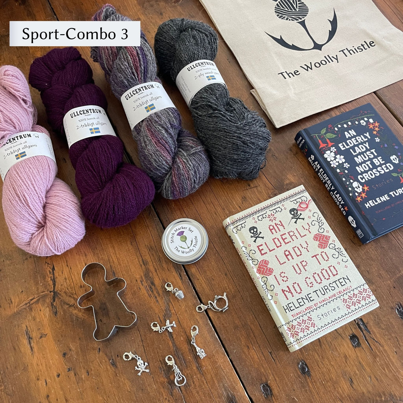 The Swedish Book Bundle components which include two books by Helene Tursten, TWT Tote bag, Stitch marker set, gingerbread cookie cutter, and Ullcentrum Sport Weight yarn. Components are shown and laid out on table. Yarn colors in Sport Combo 3 include pink, deep purple, variegated grey, and dark grey.