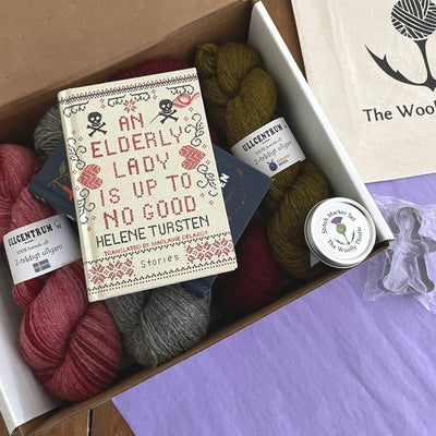 The Swedish Book Bundle components which include two books by Helene Tursten, TWT Tote bag, Stitch marker set, gingerbread cookie cutter, and Ullcentrum Worsted Weight yarn. Components are shown in box.