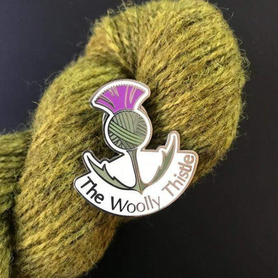 The Woolly Thistle Enamel Pin against a skein of green yarn.