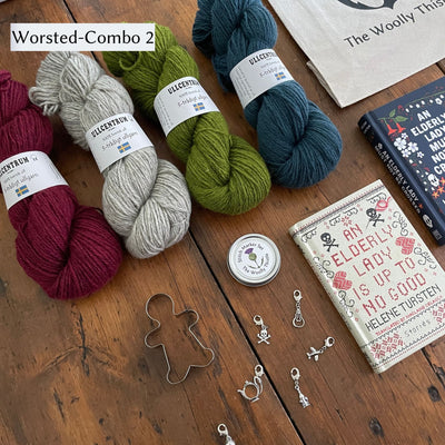 The Swedish Book Bundle components which include two books by Helene Tursten, TWT Tote bag, Stitch marker set, gingerbread cookie cutter, and Ullcentrum Worsted Weight yarn. Components are shown and laid out on table. Yarn colors included in Worsted Combo 2 include deep red, light grey, spring green, and blue. 